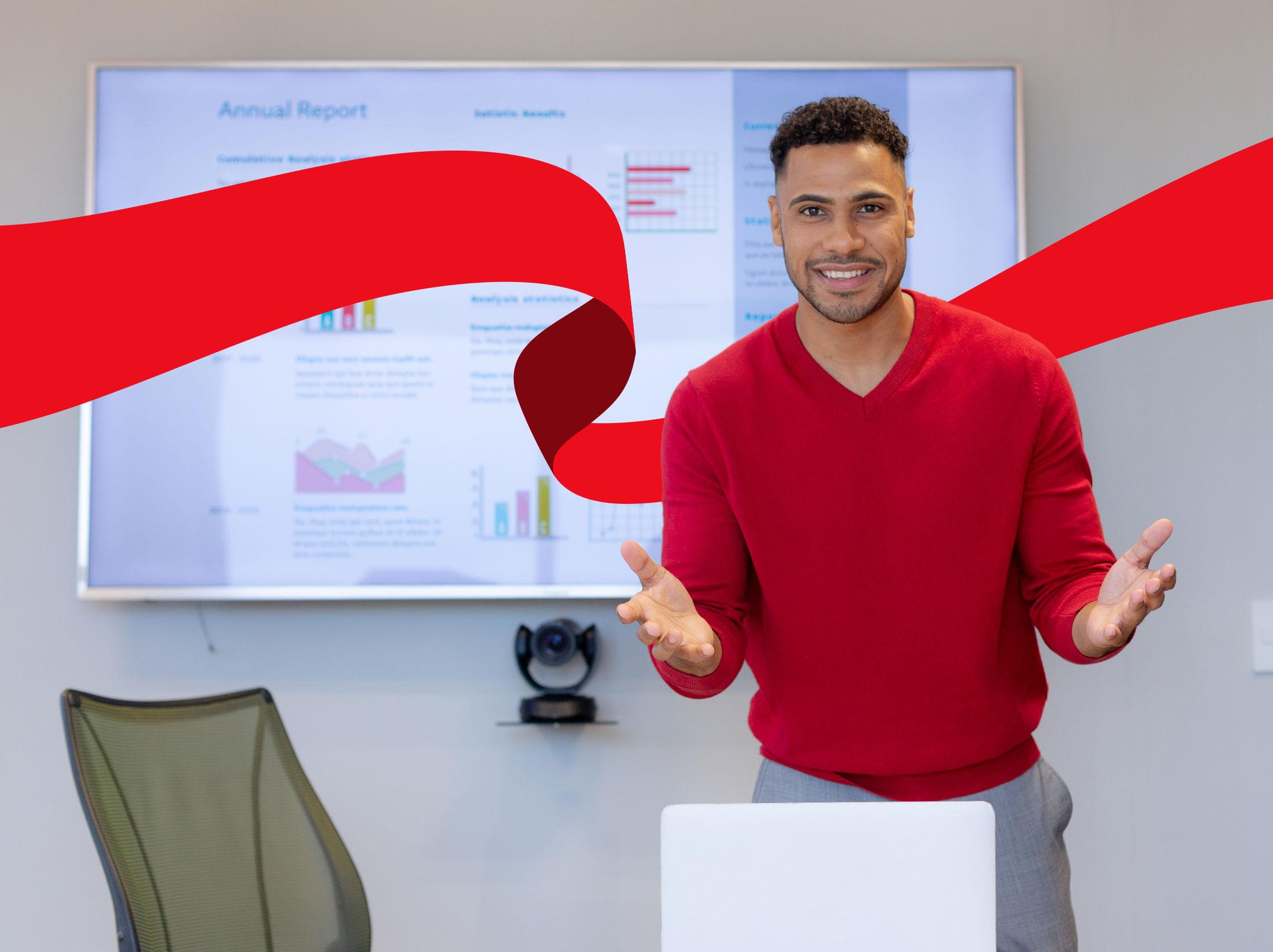 Business professional standing and presenting in front of a large monitor with data and graphs on it in a business setting.