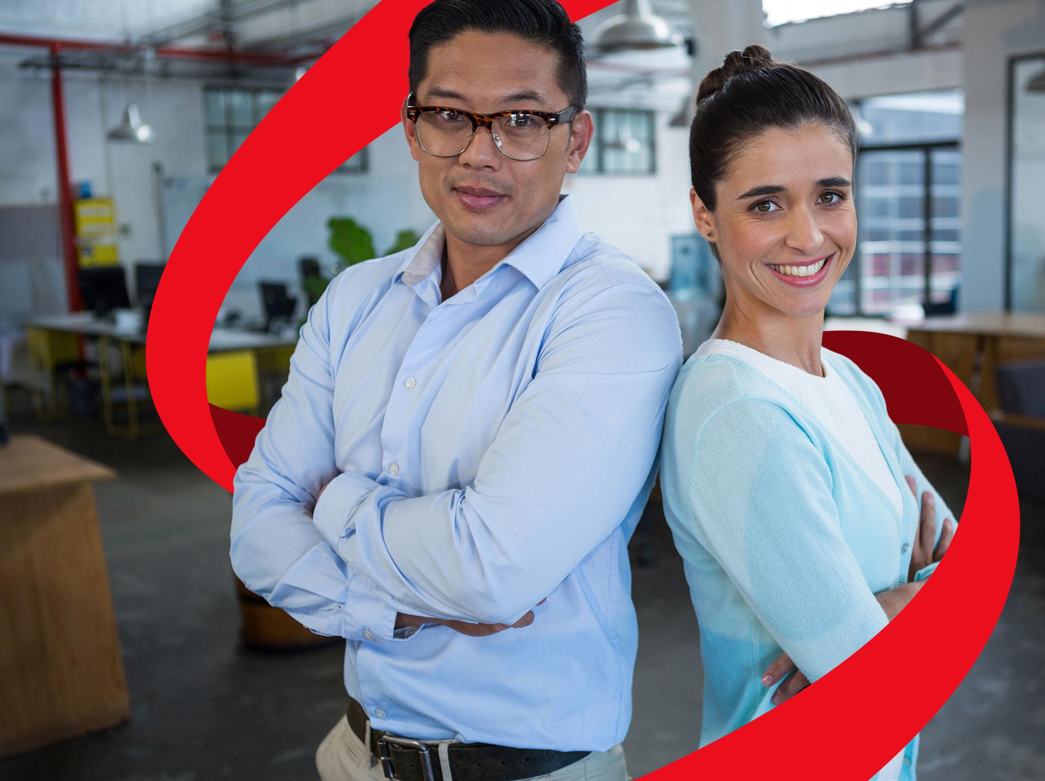 Two business professionals standing back to back in an office setting.  They are smiling.